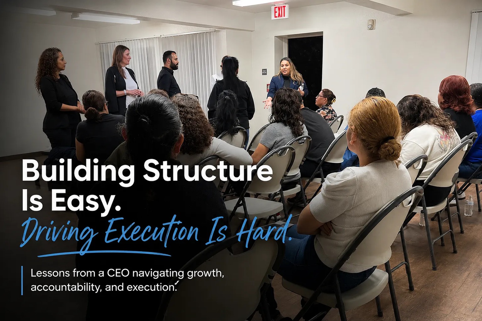 A team meeting in a community room. Sheila Greene and colleagues stand at the front while a speaker addresses seated staff, beneath the headline Building Structure Is Easy. Driving Execution Is Hard.