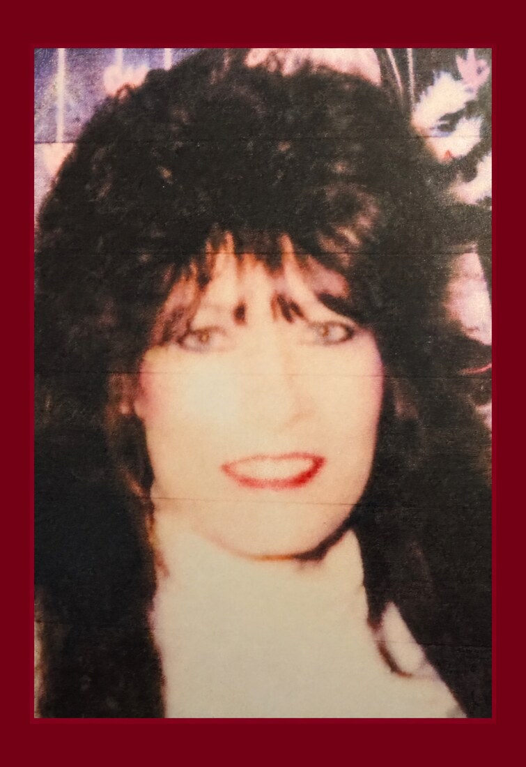 Mama Rose in the 1980s wearing dramatic dark hair, eyeliner, red lipstick, and earrings